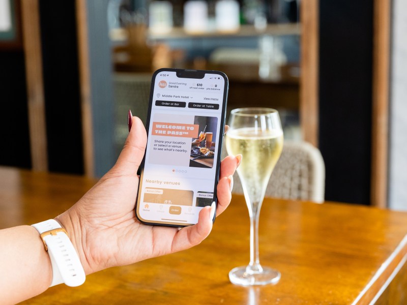 Woman holding up a smartphone with The Pass app open, with a glass of champagne in the background on a table.