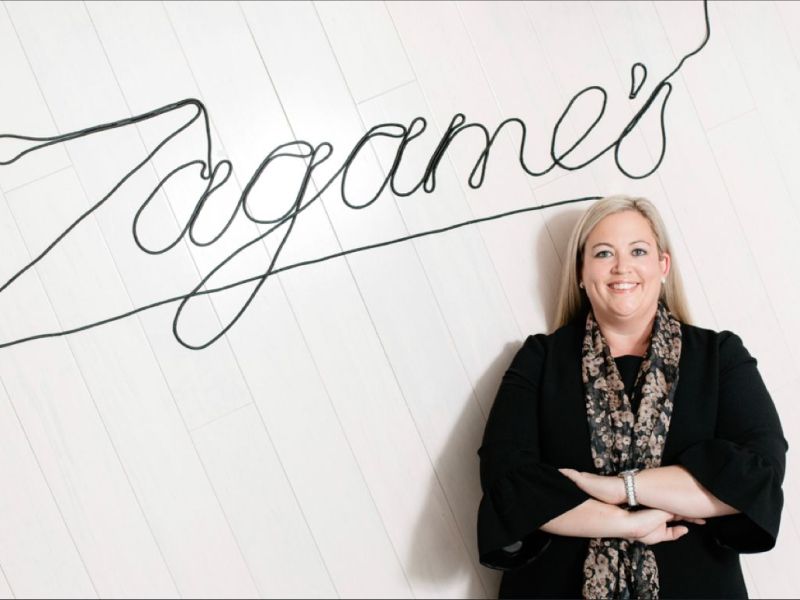 A woman standing in front of a sign that says Zagames with her arms crossed.