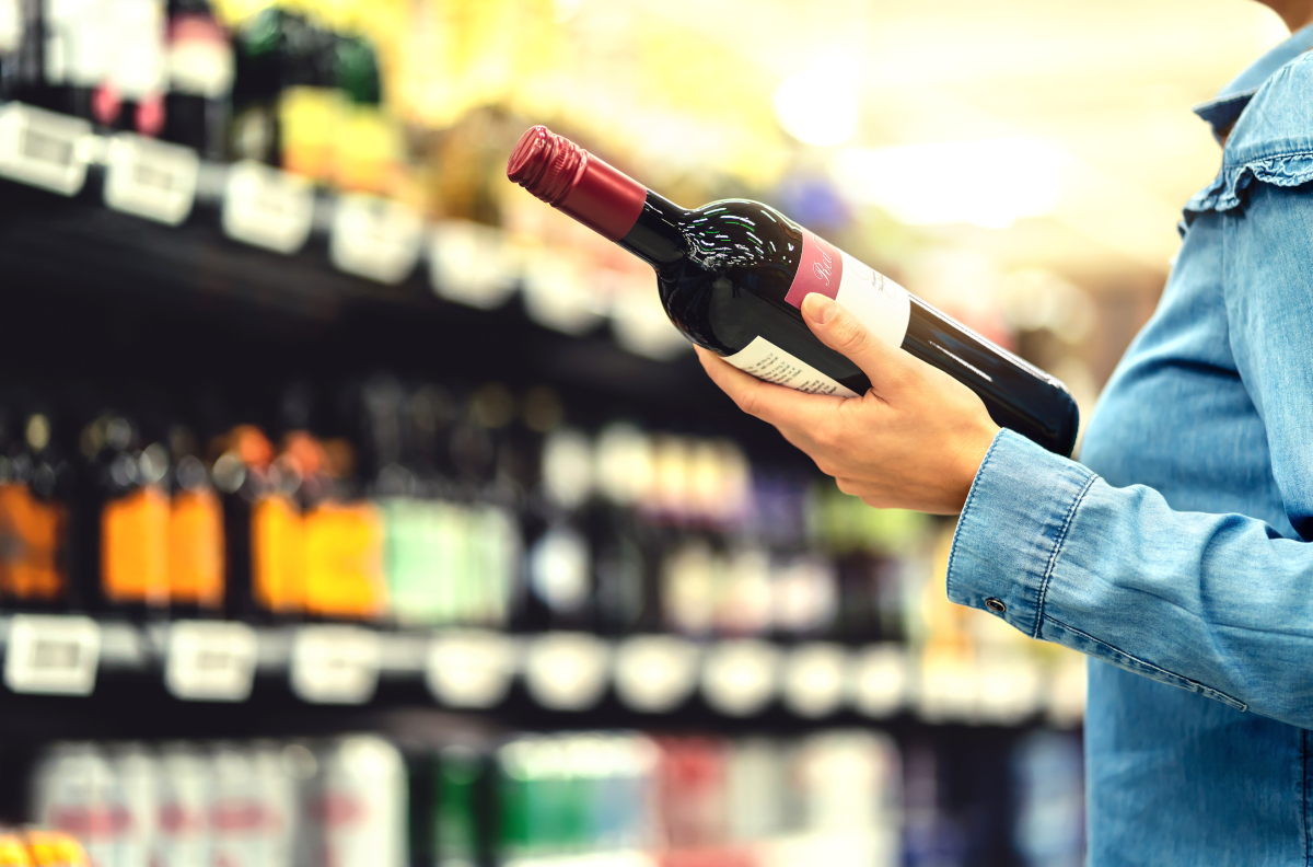 A woman holds a bottle of wine in a bottle shop