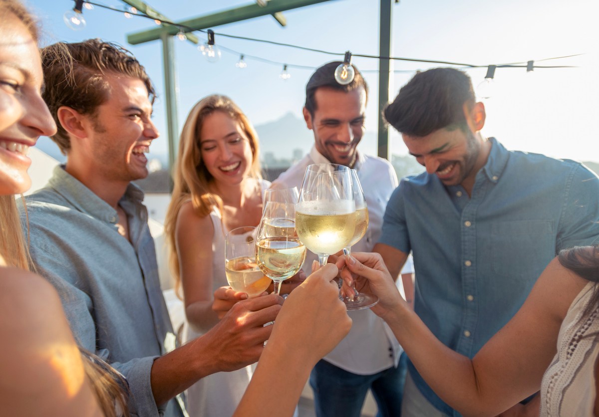Group of friends having drinks at sunset. They are celebrating with a wine toast. They are drinking white wine. They are smiling, laughing and having fun.