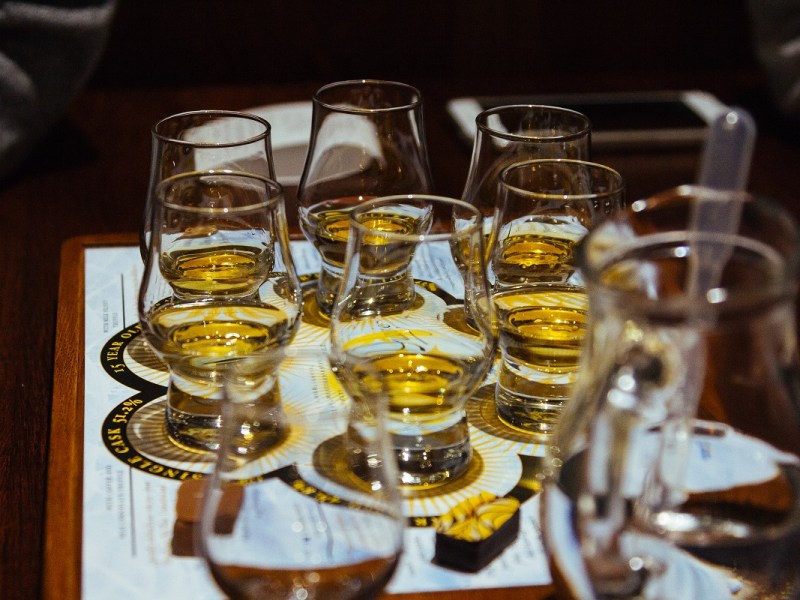A set of six small glasses is set out ready for a whisky tasting flight. The glasses are on a sheet of paper and there is a jug of water in the foreground.
