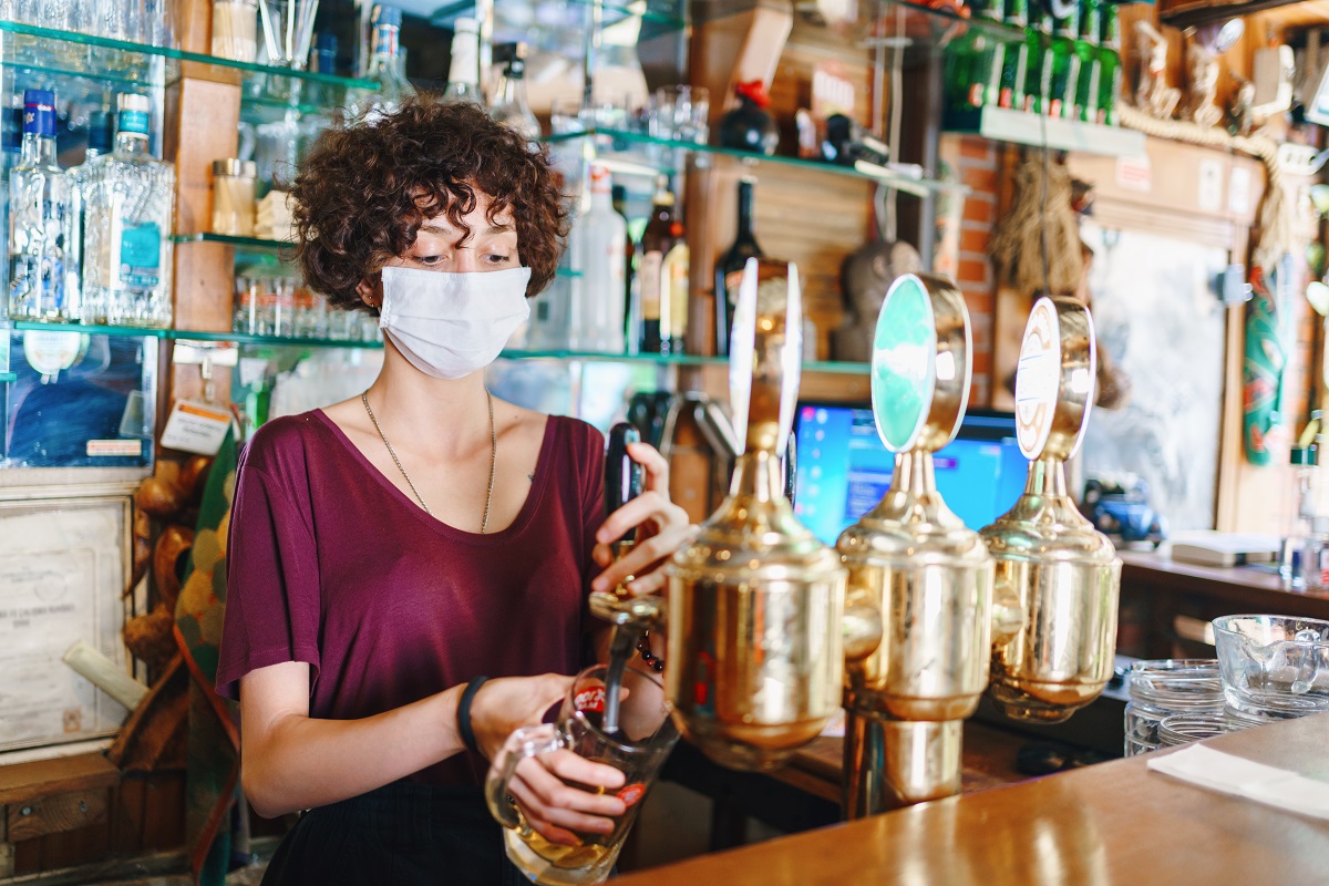 bartender with a face mask pouring a beer