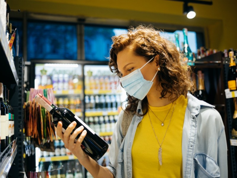 retail restrictions lockdwon - customer wears mask while choosing wine