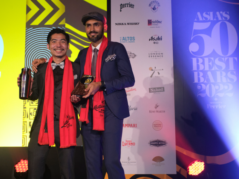 Two men from Coa staff on a stage with a colourful background, receiving their award for the Best Bar in Asia.