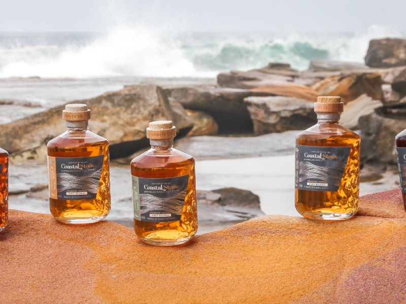 Coastal Stone range of whisky bottles at a beach with crashing waves in background