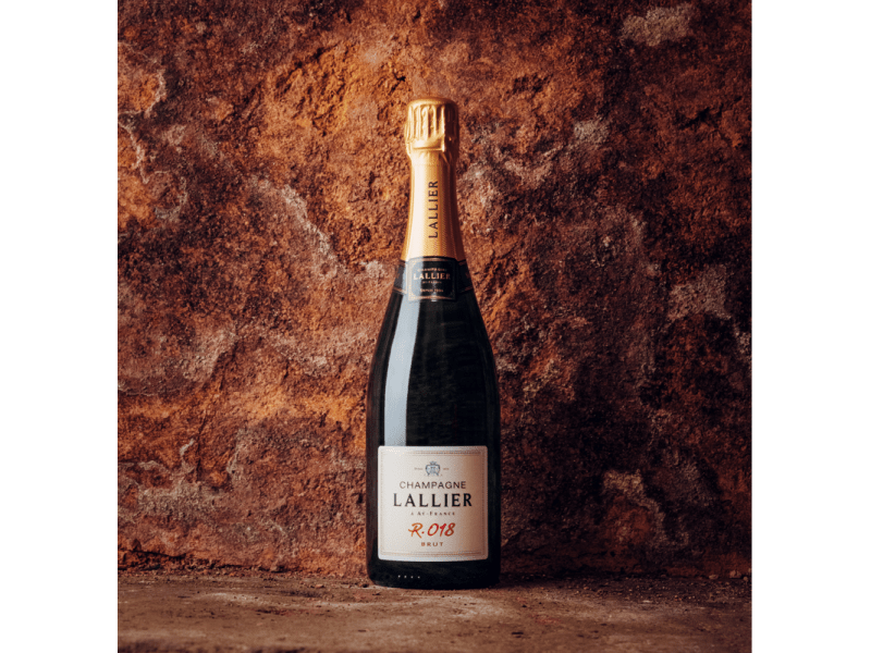 A bottle of Lallier champagne against a brick wall background